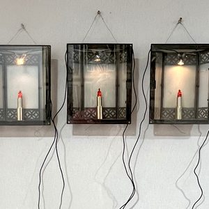 Lipstick Buddha, 1996 – Three illuminated display boxes containing Buddha figures hand-carved directly into lipstick.